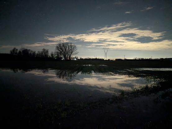 Night photo of a countryside field with a large puddle and the reflex of a few clouds