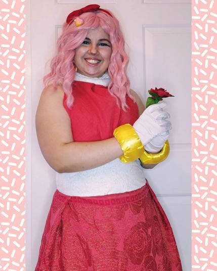 Fairy smiling at the viewer, dressed in cosplay identical to Amy's outfit, except she holds a red rose.