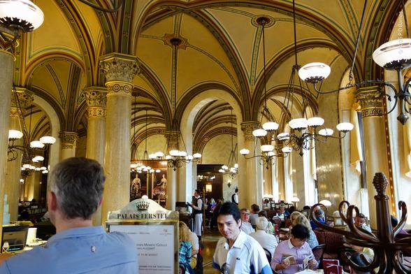 Cafe interior with columns, arches, vaulted ceiling and abundant candelabras hanging from each vault.
