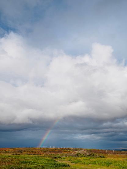Clouds in the distance with a rainbow reaching the horizon below them