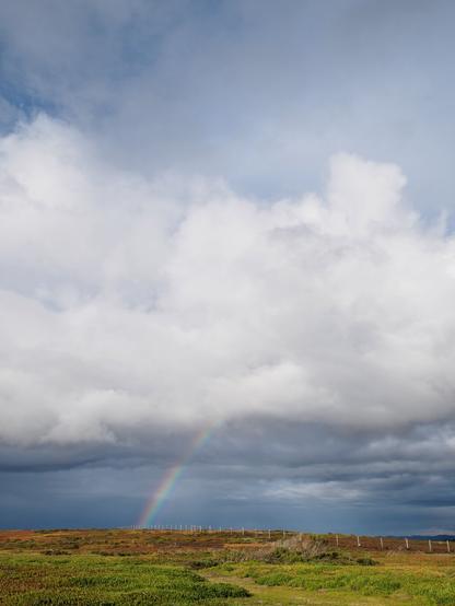 Clouds in the distance with a rainbow reaching the horizon below them