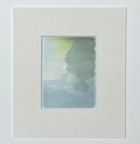 A polaroid transfer onto Arches Platine paper showing a large rock on the right, splashing water in the middle and a seemingly calm shoreline at the bottom. Mounted
