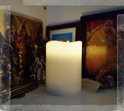 Retro-Farbfoto einer gelbweißen elektrischen Kerze, die eine Ecke mit mehreren hinduistischen Bildern erleuchtet und sich in dem Bild rechts daneben spiegelt. Sony Xperia Z5 mit Vignette for Android, soeben aufgenommen und auf dem Telefon etwas bearbeitet.