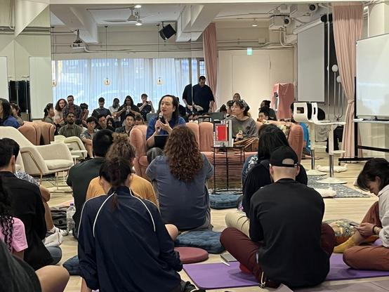 Audrey Tang holding a microphone sitting on a sofa, with participants seating on yoga mats around