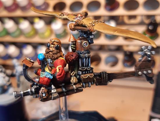 Die bemalte Figur stellt eine Flugmaschine dar. Auf ein schmales Hokzkonstrukt wurde am Bug eine kleine Kanone montiert dahinter sitzt auf einem kleinen Fellsitz ein Zwerg mit Flugbrille, hält einen Steuerknüppel mit einer Hand fest. In der anderen hält er wurfbereit eine kleine Kugelbombe mit Lunte. Hinter ihm ist ein Dampfofen montiert, der oben in einem zweiblättrigen Rotor endet. Am Heck dreht sich ein großes Zahnrad. Die Miniatur steckt auf einem kleinen durchsichtigen Ständer.