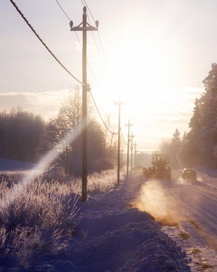A sunny winter day with everything covered in frost and snow. Two cars driving on an empty road.