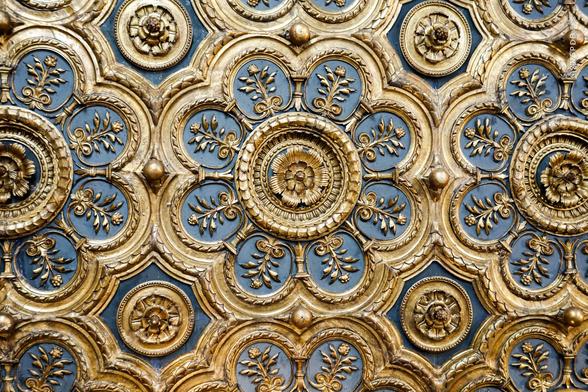 Detail of extremely ornate patterned ceiling in blue background and gilt relief. The basic pattern is an eight-rounded-petal stylised flower, each petal containing within it a smaller complete plant with leaves and a flower against the blue background, and a circular eight-petalled rosette in the centre. These touch on four sides, the concave gaps left being filled by another circular rosette.