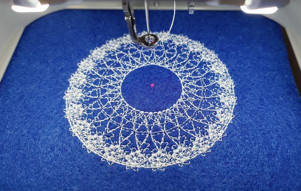 A beautiful and intricate pattern stitched in white thread on blue felt.