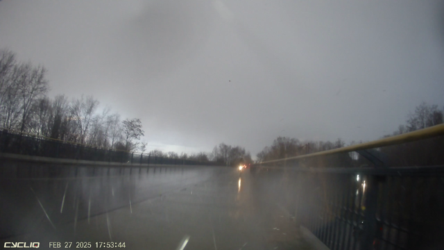 Zweirichtungsradweg bei Regen & Hagel auf einer Brücke mit Radfahrer im Gegenverkehr. Rechts ein hohes Geländer. Links ein sehr hoher Bordstein.
