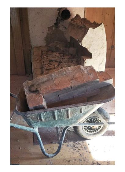 A demolished old oven in pieces of fireclay bricks. Wheelbarrow loaded with with corner brickpart. Wooden old paneling in the background.