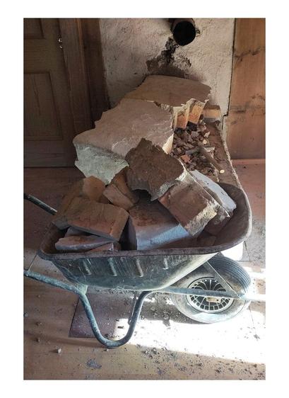 A demolished old oven in pieces of fireclay bricks. Wheelbarrow loaded with brick parts. Wooden old paneling in the background.
