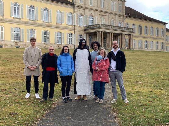 A group of people, all smiling into the camera, standing in front of the castle of Hohenheim. The picture is quite boring at first sight, but then you realise that the person in the middle is wearing a costume... 

From left to right: Simon Leoz, Mira Baer, Franziska Koch, Peter the Penguin, Dimitrios Nakos, Korinna Allhoff (with her little coworker in the carrier) and Rémi Legrand.