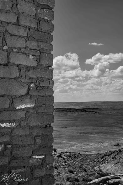 An ancient Native American stone wall stands vertical against a cloudy sky and rocky desert landscape at Hovenweep.