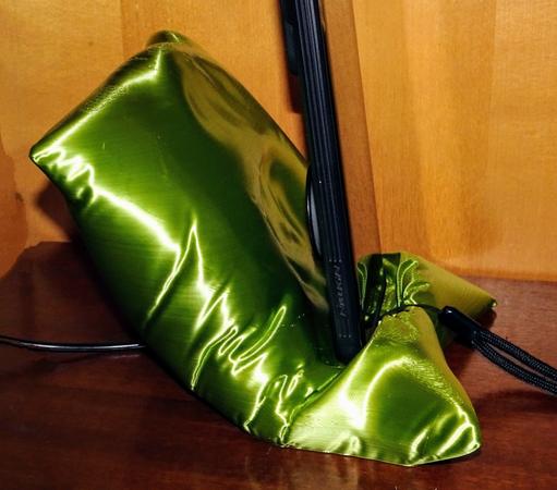 photo showing the, metallic green, phone stand pillow from the side with a smartphone about to fall into it's comfy embrace. You can see that the form of the pillow fits both the popsocket on the back of the phone-case as well as the pixel phone's bulging camera.