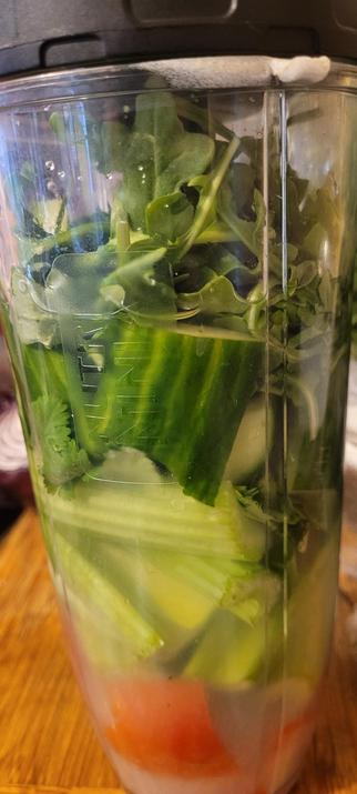 A Ninja blender cup with baby arugula, celery Roma tomato, cilantro, lime and lemon juice before being blended.