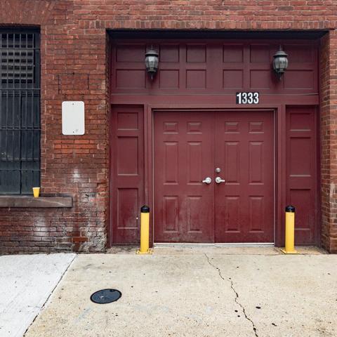 A yellow plastic cup on the windowsill of outside a building next to a garage door with two yellow barricades