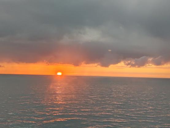 Picture of the sun rising over the Welsh coastline. Some large dark clouds in the foreground overshadow the rising sun.