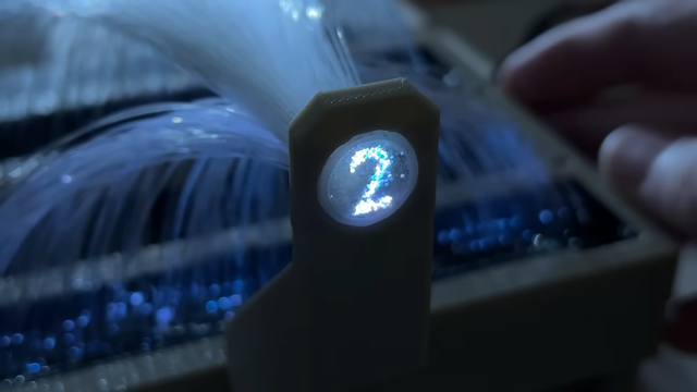 <div><img alt="" class="attachment-large size-large wp-post-image" height="450" src="https://hackaday.com/wp-content/uploads/2025/02/The-Fibrovisor-4-46-screenshot.png?w=800" style="margin: 0 auto; margin-bottom: 15px;" width="800" /></div><p>If you&#8217;ve ever seen those cheap LED fiber optic wands at the dollar store, you&#8217;ve probably just thought of them as a simple novelty. However, as [Ancient] shows us, <a href="https://www.youtube.com/watch?v=zz59e1wWyVc" target="_blank">you can turn them into a surprisingly nifty little display</a> if you&#8217;re so inclined.</p>
<p>The build starts by removing the fiber optic bundle from the wand. One end is left as a round bundle. At the other end, the strands are then fed into plastic frames to separate them out individually. After plenty of tedious sorting, the fibers are glued in place in a larger rectangular 3D-printed frame, which holds the fibers in place over a matrix of LEDs. The individual LEDs of the matrix light individual fibers, which carry the light to the round end of the bundle. The result is a tiny little round display driven by a much larger one at the other end.</p>
<p>[Ancient] had hoped to use the set up for a volumetric display build, but found it too fragile to be fit for purpose. Still, it&#8217;s interesting to look at nonetheless, and a good demonstration of how fiber optics work in practice. As this display shows, you can have two glass fibers carrying completely different wavelengths of light righ