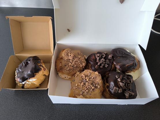 6 gros choux à la crème : deux avec des morceaux de chocolat sur le sommet, deux au caramel avec des morceaux de snickers et deux au chocolat fourré à la confiture de myrtilles.