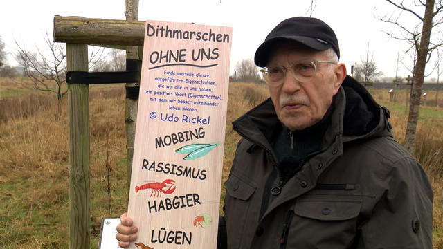 Ein älterer Herr steht neben einer Tafel mit dem Schriftzug "Dithmarschen ohne uns". © NDR