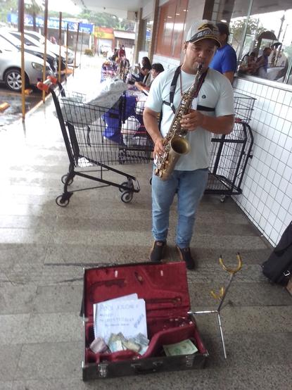 Imagem do músico tocando saxofone na porta do supermercado.