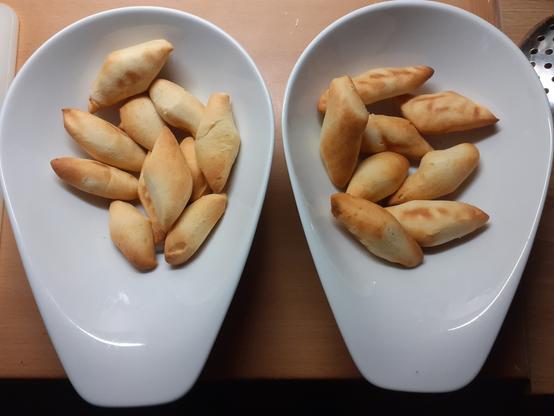 Zwei weiße Keramik Schüsseln nebeneinander mit jeweils Schmalzgebäck ohne Puderzucker drinnen.