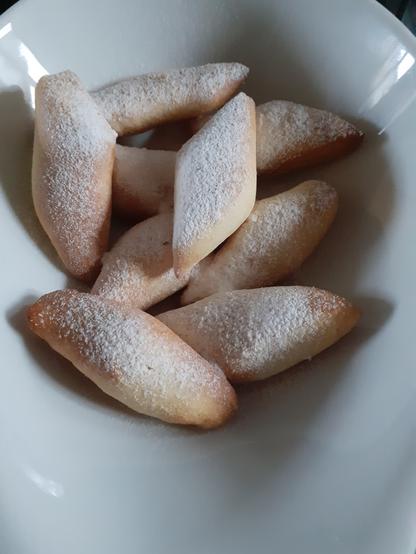 Schmalzgebäck mit Puderzucker in einer weißen Keramik Schüssel.