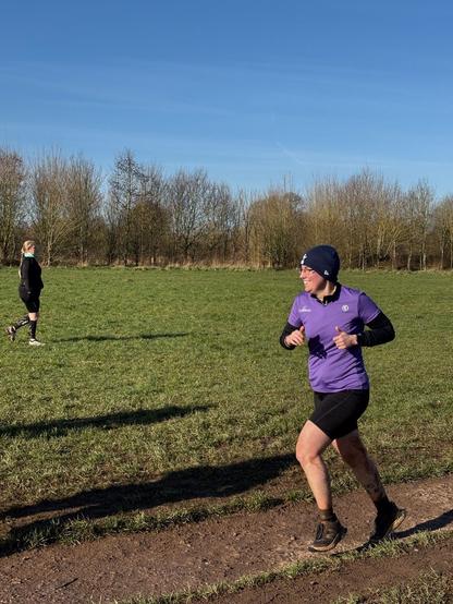 Emily smiling, wrapped up against the cold, wearing her purple 25 volunteer tshirt and with blue sky above.