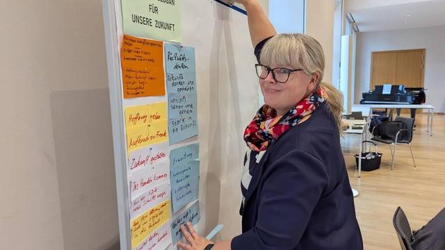 Berit Hartmann klebt bunte Zettel an eine Moderationswand und schaut in die Kamera