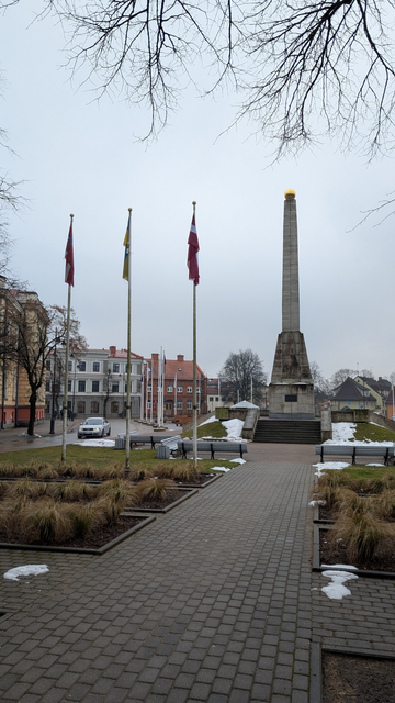 Cēsis, Vienības laukums, skats uz karogiem, ēkām un pieminekli.