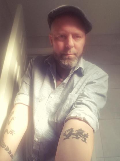 Me wearing a Yorkshire flat cap and smart shirt, showing upper, inner forearm with highly stylized "tribal" Welsh dragon in jet black ink.

The image has the "nostalgia" filter on it to make it appear to be an old pic. I took it 10 minutes ago.