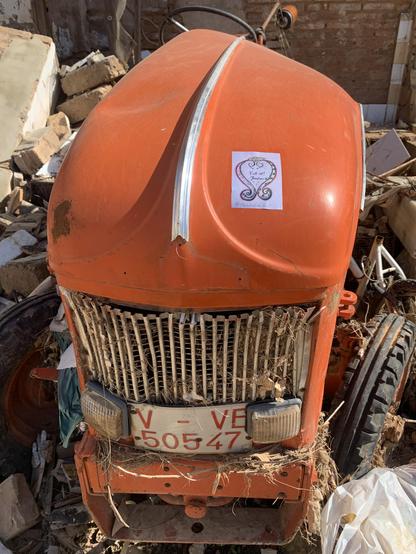 Un tractor de color naranja destrozado por la riada del 29 de noviembre de 2024 en l'horta sud de València. A su alrededor escombros de una casa de Catarroja con una pegatina que exige Mazón Dimisión.