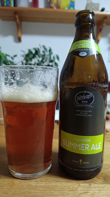 Auf einem Holztisch steht ein mit braunem Bier gefülltes Glas und daneben eine Bierflasche
