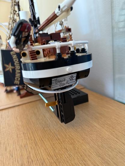 A close-up of a model ship, specifically the "Black Pearl," with a figure resembling a pirate. The ship features a white and black hull, and a sign marked "ENDURANCE" is visible in the foreground.