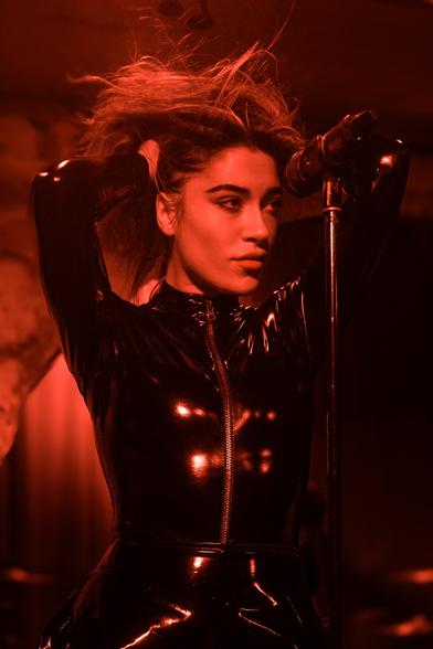 A woman holding her hair up while performing. The room is awash with red light.
