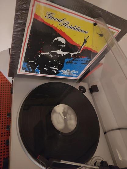 record player playing Good Riddance - ballads from the revolution LP, in the background is the cover, showing an soldier from the back, making the victory sign with his finger