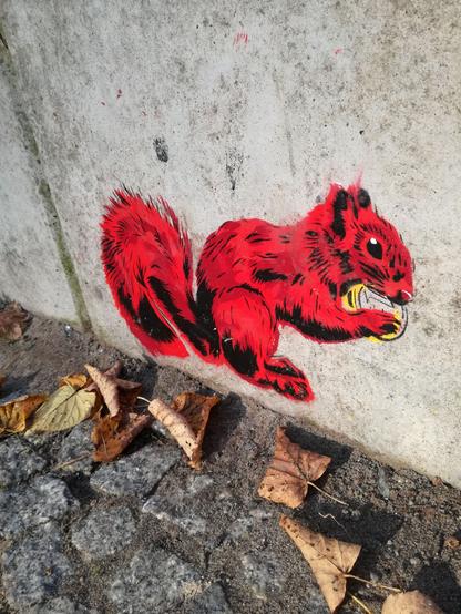 Streetart. Auf Wand unten ein rotes Eichhörnchen, das einen Euro frisst. Davor Kopfsteinpflaster und trockenes Laub