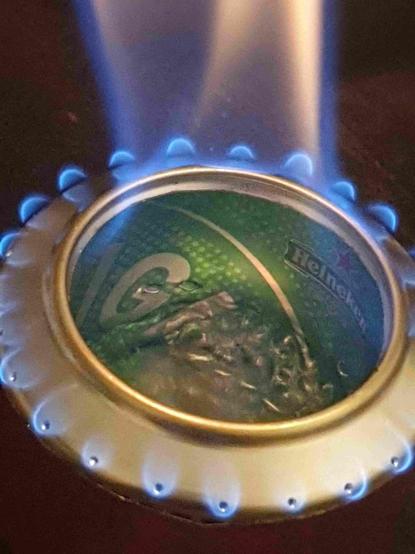 Réchaud à alcool en canette alu de 33cL.
On voit l'alcool en ébullition et les flammes sortant par des trous disposés sur tout le pourtour d'un cul de canette découpé et troué.