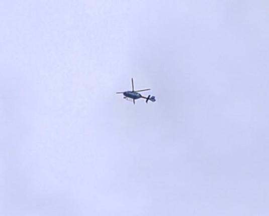Un helicóptero flota muy alto en el cielo, se recorta como una figura oscura contra las nubes.