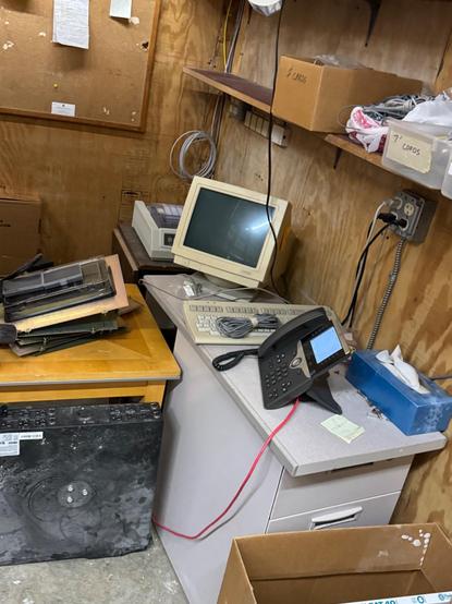 A very old mono CRT PC display with old keyboard in the corner of a network closet, long unused