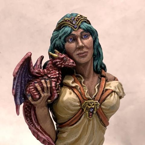Bust of a woman holding a small pink and indigo dragon up to her face as if listening to it whisper. They look off to the right. She has long, silky teal hair, blue eyes, and wears a cream-colored frilly shirt. Over the shirt is a red leather harness with a gold medallion over her heart. She also wears a gold tiara.