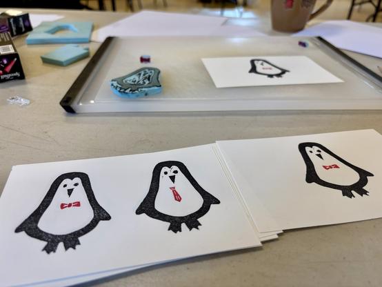Block prints of penguins in various ties with the rubber stamp used visible in the background.