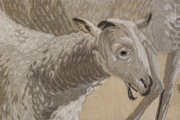 Very close view of a small section of a wall hung tapestry, featuring a sheep's head and part of its body. Although individual knots can be seen, the amount of tonal variation and detail is amazing, even though its rendered with a palette of entirely beiges and browns.