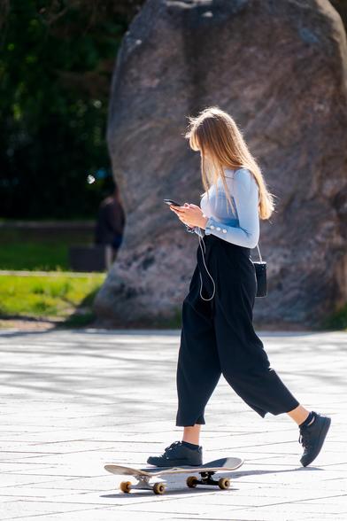A girl walking on the street and typing on a phone. There's a skateboard on the pavement and photo composed so that it looks like this girl is going to step on a skateboard without noticing.
