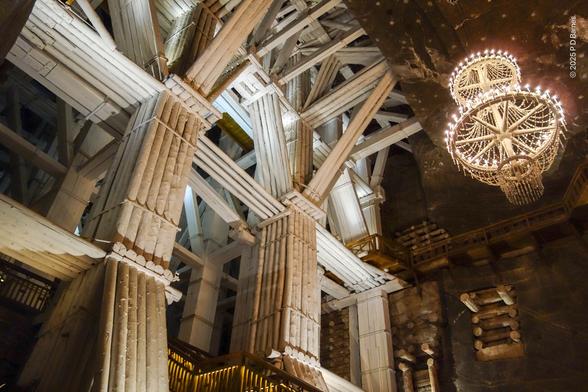 A literal forest of massed tree trunk timbers, bound together into huge buttresses as pillars and shoring inside the Wieliczka salt mine. This view alone would contain hundreds of massed timbers in complex pillars, beams and struts. For incongruity, there is also a salt-crystal chandelier providing some light.