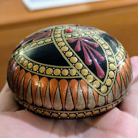 A photo showing the side of the stone, showing a decorative "band" made of copper and antique bronze painted swooshes, bordered by gold dots. This band runs around the sides of the stone, and under the points of the triquetra knot on top.