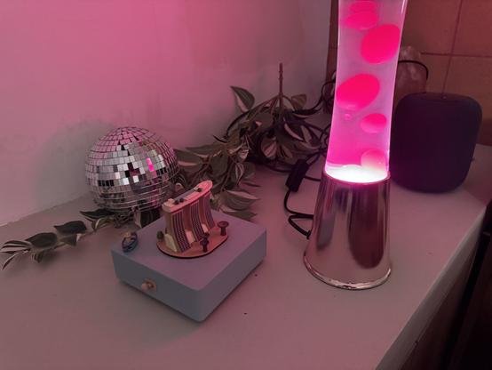 Un pot de fleur disco ball, une miniature japonaise représentant une tour et des bateaux, un faux liège, un HomePod et une lava lampe en vrac sur un banc en béton suite à notre déménagement