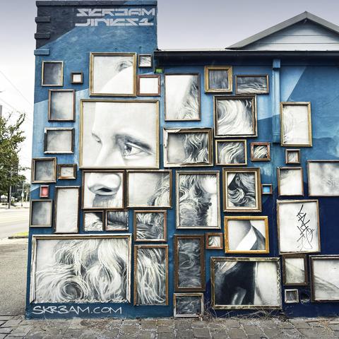 A wall of an old building with a black and white painting of a 19th century man with a large beard, but it’s split up into separate, differently-sized sections, all framed.
