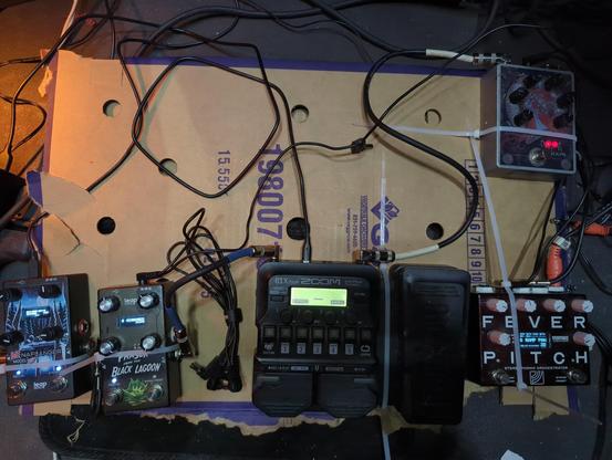 bass / guitar effects pedal board made out of cardboard with zip ties holding each in place.
