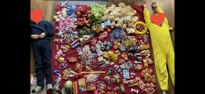 Eine Rote Decke komplett bedeckt mit Süßigkeiten. Links und rechts davon liegen zwei Kinder